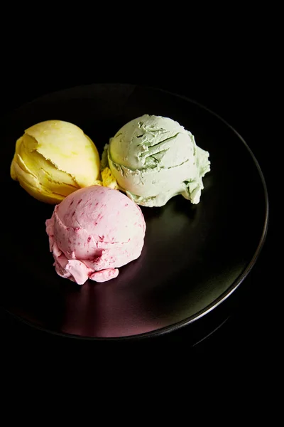 Deliciosas bolas de helado amarillo, rosa y verde en plato aislado en negro - foto de stock