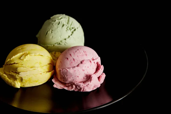 Deliciosas bolas de helado amarillo, rosa y verde en plato aislado en negro - foto de stock