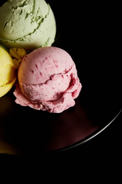 Deliciosas bolas de helado amarillo, rosa y verde en plato aislado en negro - foto de stock