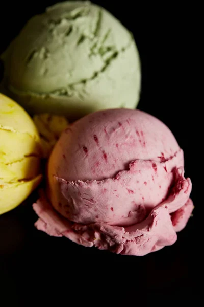 Enfoque selectivo de deliciosas bolas de helado amarillo, rosa y verde aisladas en negro - foto de stock