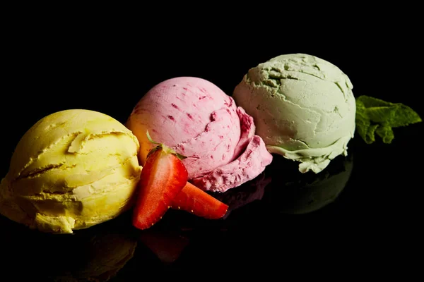 Köstliche Eiskugeln aus Zitrone, Erdbeere und Minze isoliert auf schwarz — Stockfoto