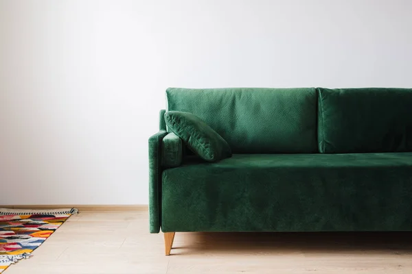 Sofá verde con almohada cerca de alfombra de colores en el suelo - foto de stock