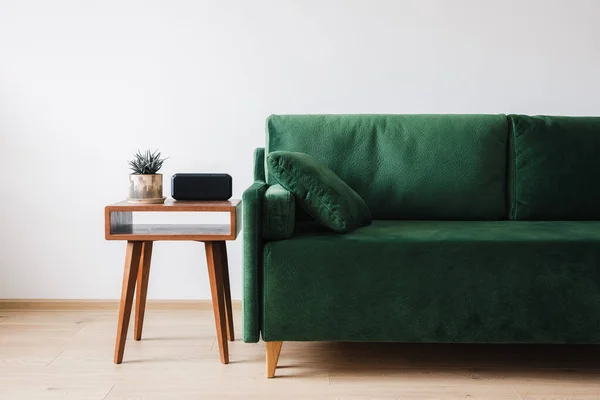 Зеленый диван с подушкой и деревянный журнальный столик с растением и будильником — стоковое фото
