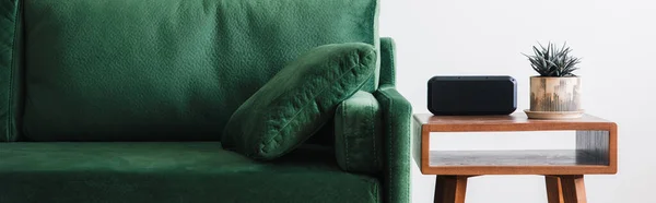 Close up view of green sofa with pillow and wooden coffee table with plant and alarm clock, panoramic shot — Stock Photo