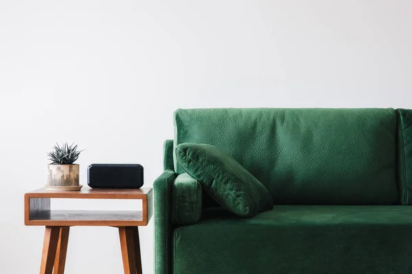 Закрыть вид на зеленый диван с подушкой и деревянным журнальным столиком с растением и будильником — стоковое фото