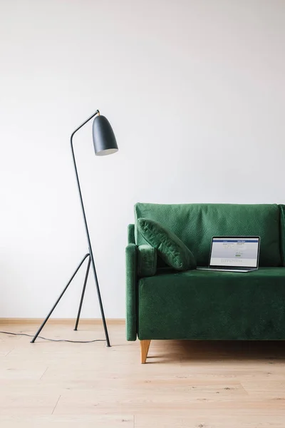 KIEW, UKRAINE - 14. APRIL 2020: grünes Sofa mit Kissen und Laptop mit Facebook-Website auf dem Bildschirm in der Nähe von Metall moderne Stehlampe — Stockfoto