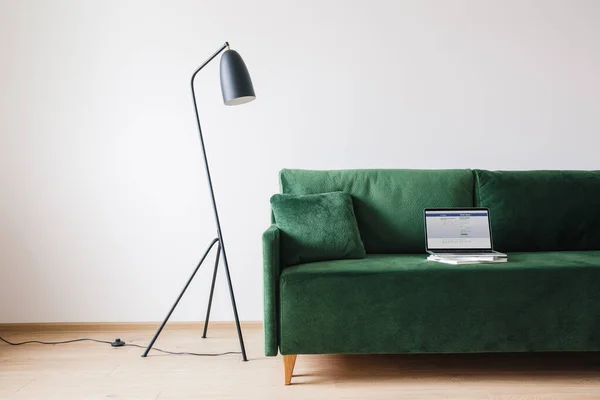 KIEW, UKRAINE - 14. APRIL 2020: grünes Sofa mit Kissen und Laptop mit Facebook-Website auf dem Bildschirm in der Nähe von Metall moderne Stehlampe — Stockfoto