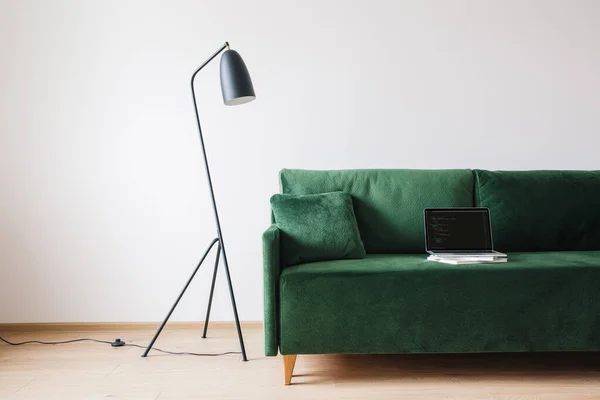KYIV, UKRAINE - APRIL 14, 2020: green sofa with pillow and laptop with javascript on screen near metal modern floor lamp — Stock Photo