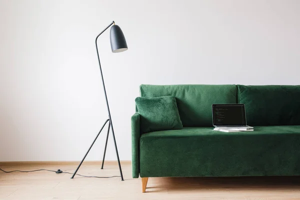 KIEW, UKRAINE - 14. APRIL 2020: grünes Sofa mit Kissen und Laptop mit Javascript auf dem Bildschirm in der Nähe von Metall moderne Stehlampe — Stockfoto