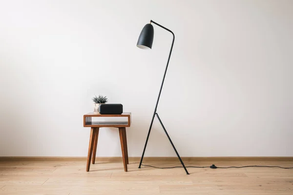 Lámpara de pie de metal y mesa de centro de madera con planta y reloj con pantalla en blanco - foto de stock