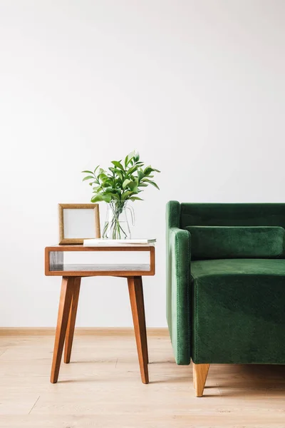 Sofá verde perto de mesa de café de madeira com planta, livros e moldura para fotos — Fotografia de Stock