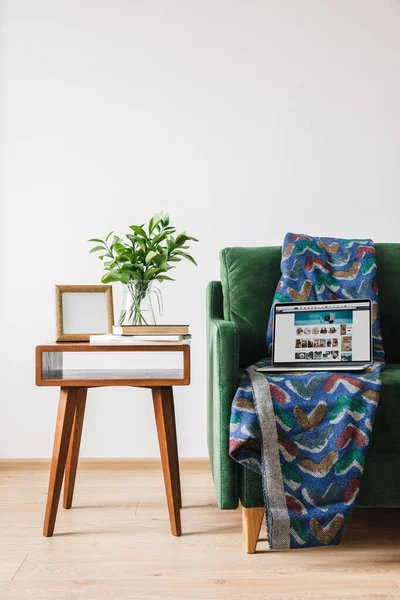 QUIIV, UCRÂNIA - 14 de abril de 2020: sofá verde com cobertor e laptop com site da amazônia perto de mesa de café de madeira com planta verde, livros e moldura para fotos — Fotografia de Stock