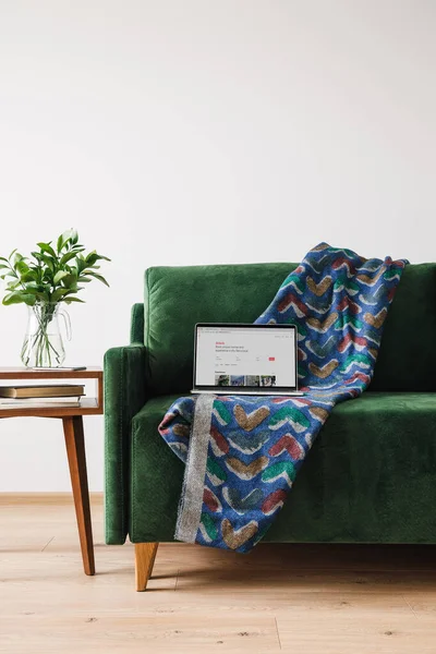 KIEW, UKRAINE - 14. April 2020: grünes Sofa mit Decke und Laptop mit Airbnb-Webseite in der Nähe eines hölzernen Couchtisches mit grüner Pflanze — Stockfoto