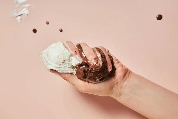 Cropped view of woman holding melted brown and white ice cream on pink background — Stock Photo