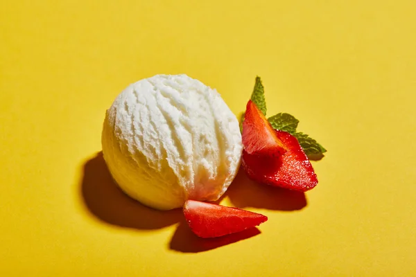 Frische leckere Eiskugel mit Minzblättern und Erdbeere auf gelbem Hintergrund — Stockfoto