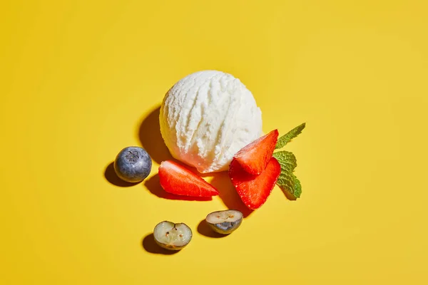 Frische leckere Eiskugel mit Minzblättern und Beeren auf gelbem Hintergrund — Stockfoto