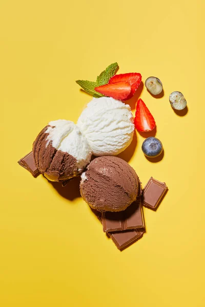 Vista superior de sabroso helado marrón y blanco con bayas, chocolate y menta sobre fondo amarillo - foto de stock