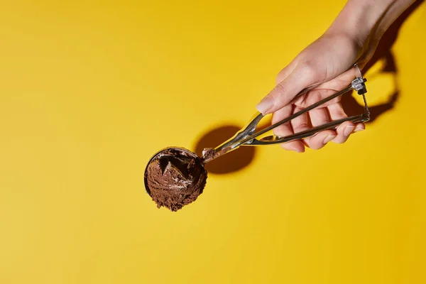 Visão parcial da mulher segurando bola de sorvete de chocolate fresco em colher no fundo amarelo — Fotografia de Stock