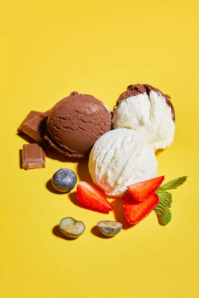 Saboroso sorvete marrom e branco com bagas, chocolate e hortelã no fundo amarelo — Fotografia de Stock