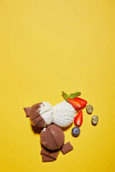 Vista superior de sorvete marrom e branco saboroso com bagas, chocolate e hortelã no fundo amarelo — Fotografia de Stock