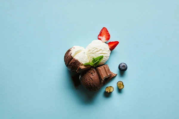Vista superior de sorvete marrom e branco saboroso com bagas, chocolate e hortelã no fundo azul — Fotografia de Stock