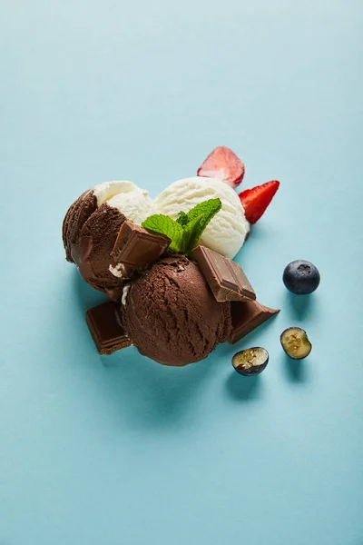 Vue de dessus de savoureuse crème glacée brune et blanche aux baies, chocolat et menthe sur fond bleu — Photo de stock