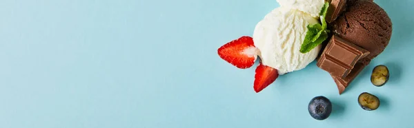 Top view of tasty brown and white ice cream with berries, chocolate and mint on blue background, panoramic shot — Stock Photo