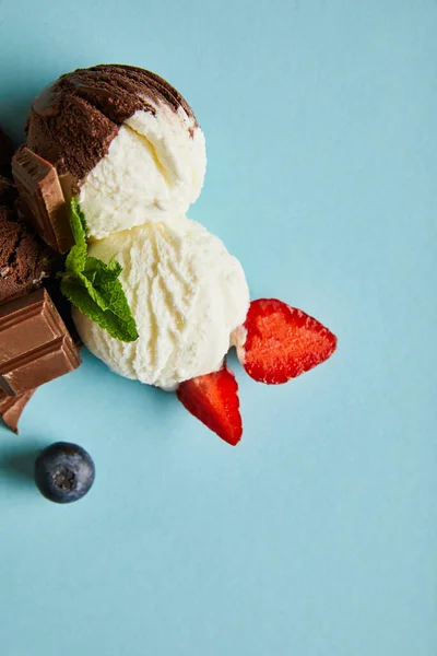 Vista superior de sabroso helado marrón y blanco con bayas, chocolate y menta sobre fondo azul - foto de stock