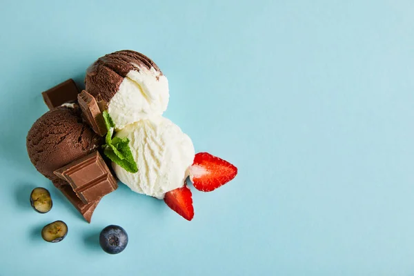 Vista superior de sabroso helado marrón y blanco con bayas, chocolate y menta sobre fondo azul - foto de stock