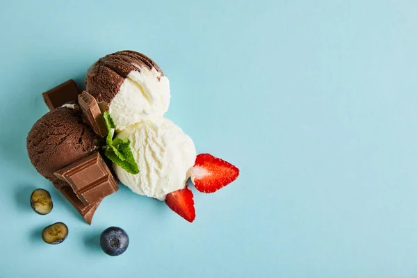 Top view of tasty brown and white ice cream with berries, chocolate and mint on blue background — Stock Photo