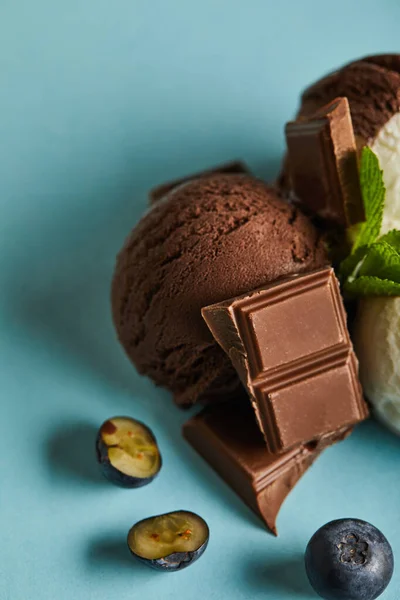 Close up view of tasty brown ice cream with berries, chocolate and mint on blue background — Stock Photo