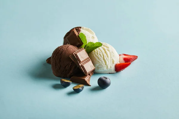 Saboroso sorvete marrom e branco com bagas, chocolate e hortelã no fundo azul — Fotografia de Stock