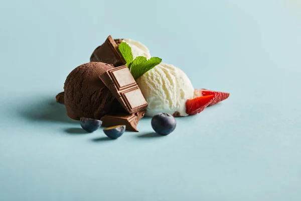 Tasty brown and white ice cream with berries, chocolate and mint on blue background — Stock Photo