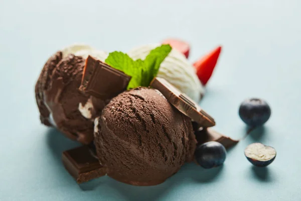 Foco seletivo de sorvete marrom e branco saboroso com bagas, chocolate e hortelã em fundo azul — Fotografia de Stock