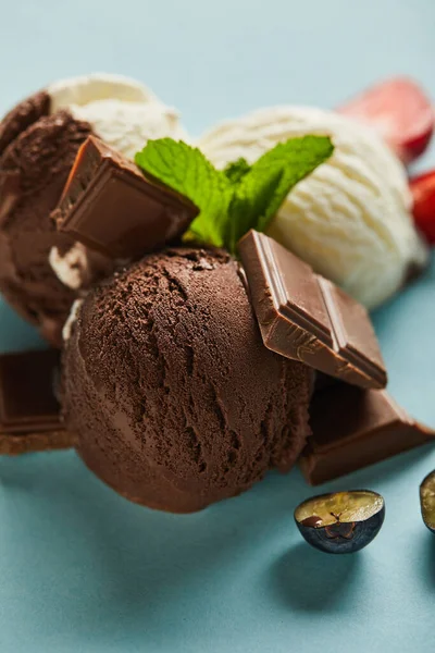 Enfoque selectivo de sabroso helado marrón y blanco con bayas, chocolate y menta sobre fondo azul - foto de stock