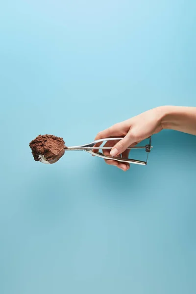 Vista recortada de la mujer sosteniendo cucharada con helado de chocolate sobre fondo azul - foto de stock