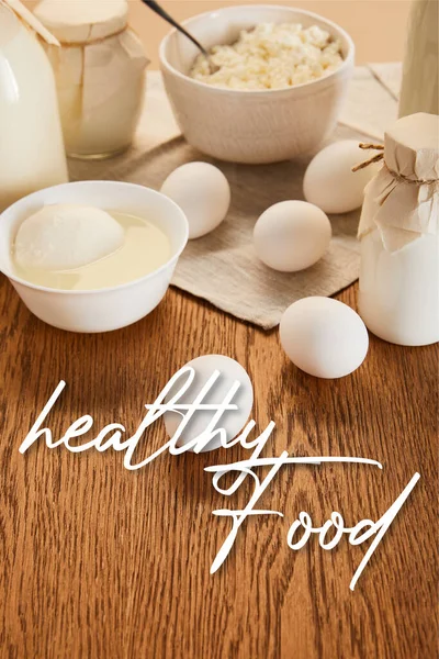 Selective focus of various fresh organic dairy products and eggs on rustic wooden table with healthy food illustration — Stock Photo