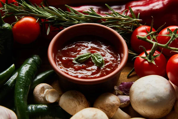 Deliciosa salsa de tomate en tazón cerca de verduras frescas maduras, romero y champiñones - foto de stock