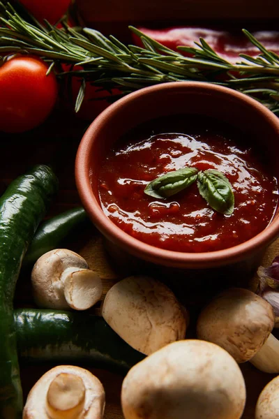 Вкусный томатный соус в миске рядом со свежими зрелыми овощами, розмарином и грибами — стоковое фото