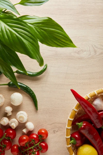 Blick von oben auf grüne Blätter und frisches reifes Gemüse in Korb auf Holztisch — Stockfoto