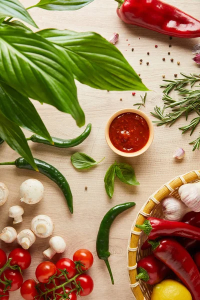 Vista superior de folhas verdes e delicioso molho de tomate em tigela perto de legumes frescos maduros, ervas, especiarias e cogumelos na mesa de madeira — Fotografia de Stock