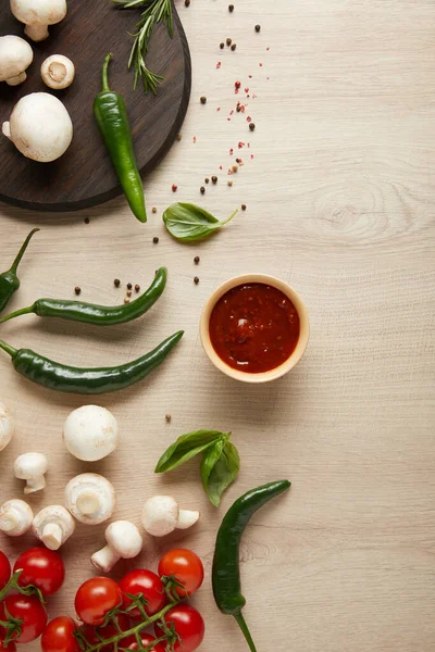 Vista superior de delicioso molho de tomate na tigela perto de legumes maduros frescos, ervas, especiarias e cogumelos na mesa de madeira — Fotografia de Stock