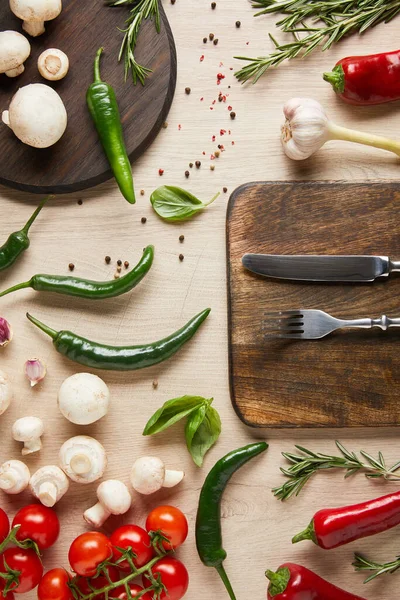 Top view of cutlery on board near fresh ripe vegetables, herbs, spices and mushrooms on wooden table — Stock Photo