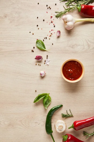 Draufsicht auf köstliche Tomatensauce in Schüssel in der Nähe von Kräutern und Gewürzen auf Holztisch — Stockfoto