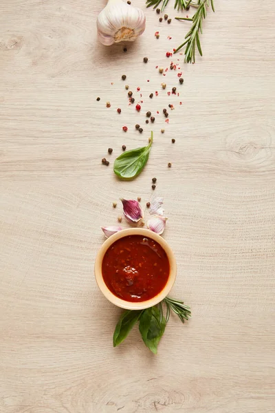 Vue du dessus de la délicieuse sauce tomate dans un bol près des herbes et des épices sur une table en bois — Photo de stock