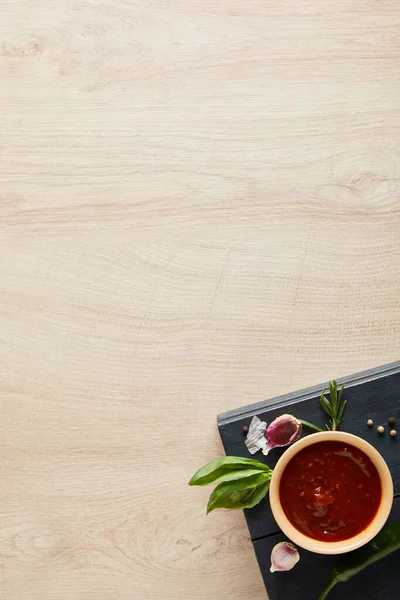 Vue du dessus de la délicieuse sauce tomate dans un bol près des herbes et des épices à bord sur une table en bois — Photo de stock