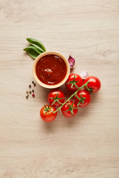 Вид на вкусный томатный соус в миске рядом со специями и помидорами на деревянном столе — стоковое фото