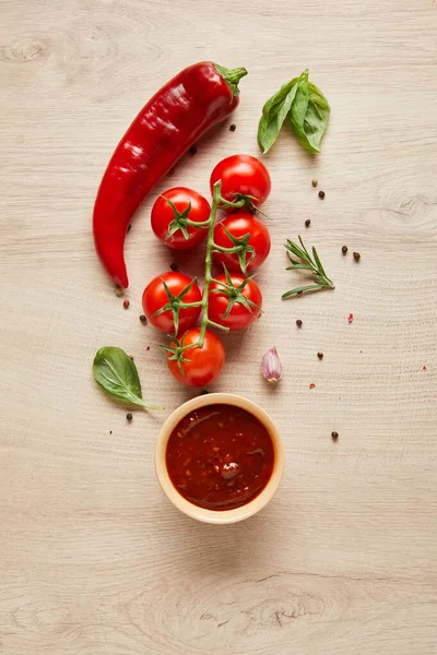 Vista superior de la deliciosa salsa de tomate en un tazón cerca de ingredientes frescos en la mesa de madera - foto de stock