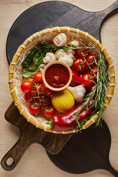 Vista superior de delicioso molho de tomate com legumes frescos maduros em cesta na mesa de madeira com tábuas — Fotografia de Stock