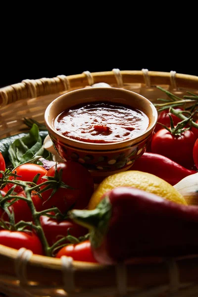 Selektiver Schwerpunkt köstlicher Tomatensauce mit frischem reifem Gemüse im Korb isoliert auf schwarz — Stockfoto